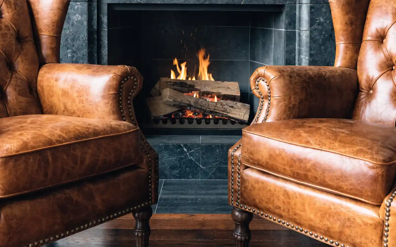 A pair of cognac leather club chairs in a refined den with a stone fireplace.