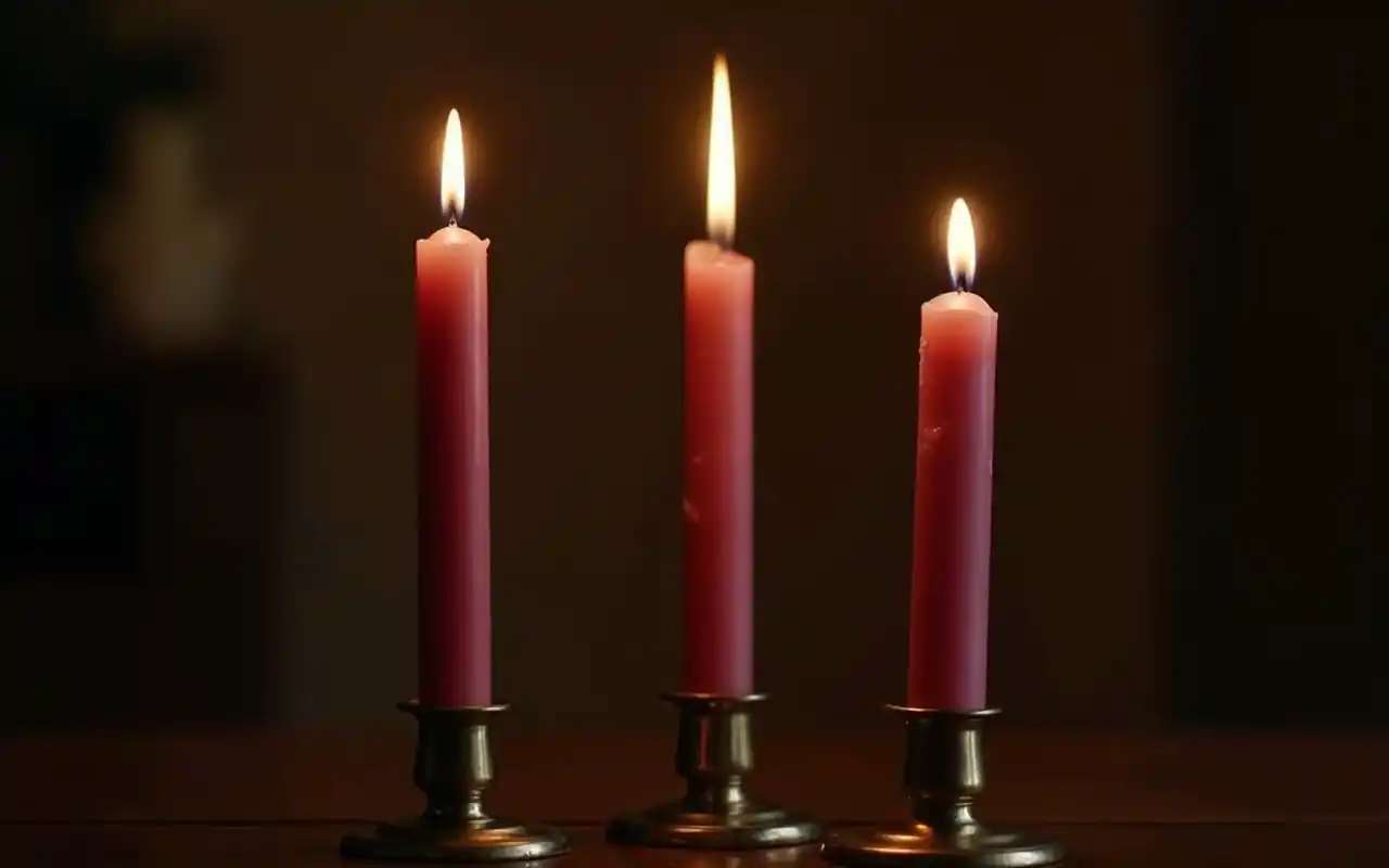 Slender pink and cream taper candles in brass holders glowing on a dark dining table.