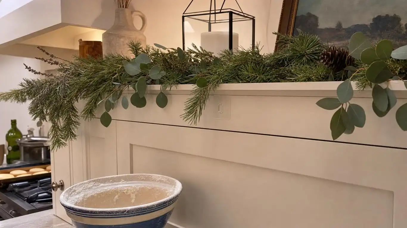 Three brass lanterns of varying heights with frosted greenery tucked between them on a kitchen island for Christmas