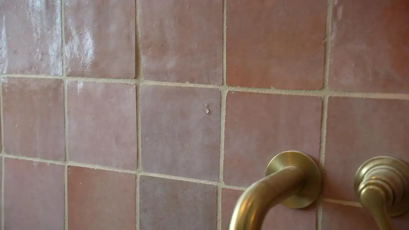 Close-up of dusty rose zellige tile bathroom wall with warm sand grout and brushed brass faucet detail