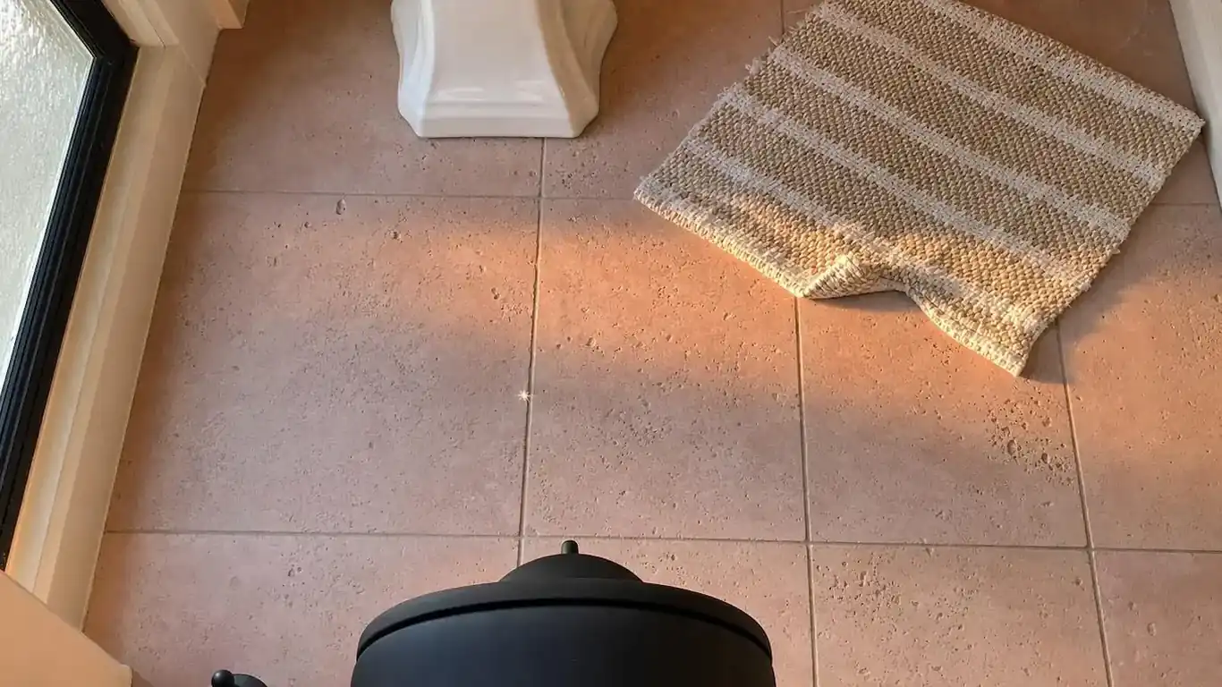 Pink travertine floor tile in honed finish inside a modern bathroom with matte black fixtures and cream walls