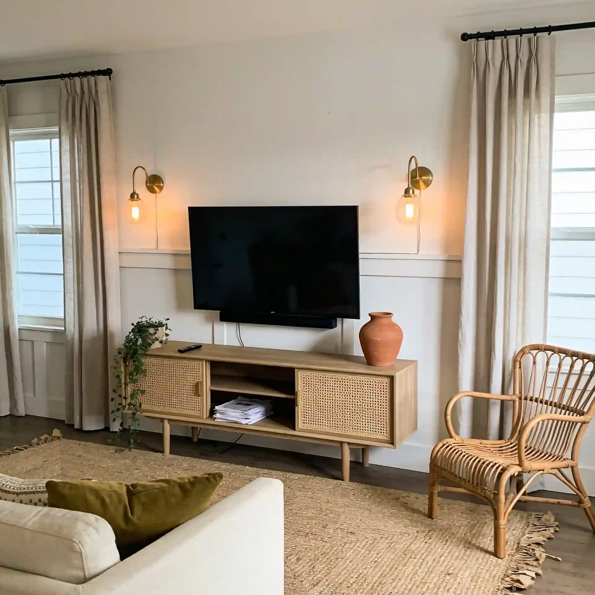 Small boho living room TV wall with cane console, wool rug, plants, and plug-in sconces