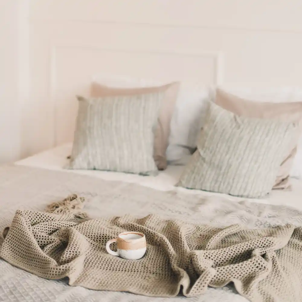 Chunky knit wool throw folded off-center at the foot of a smooth linen bed in a cozy master bedroom