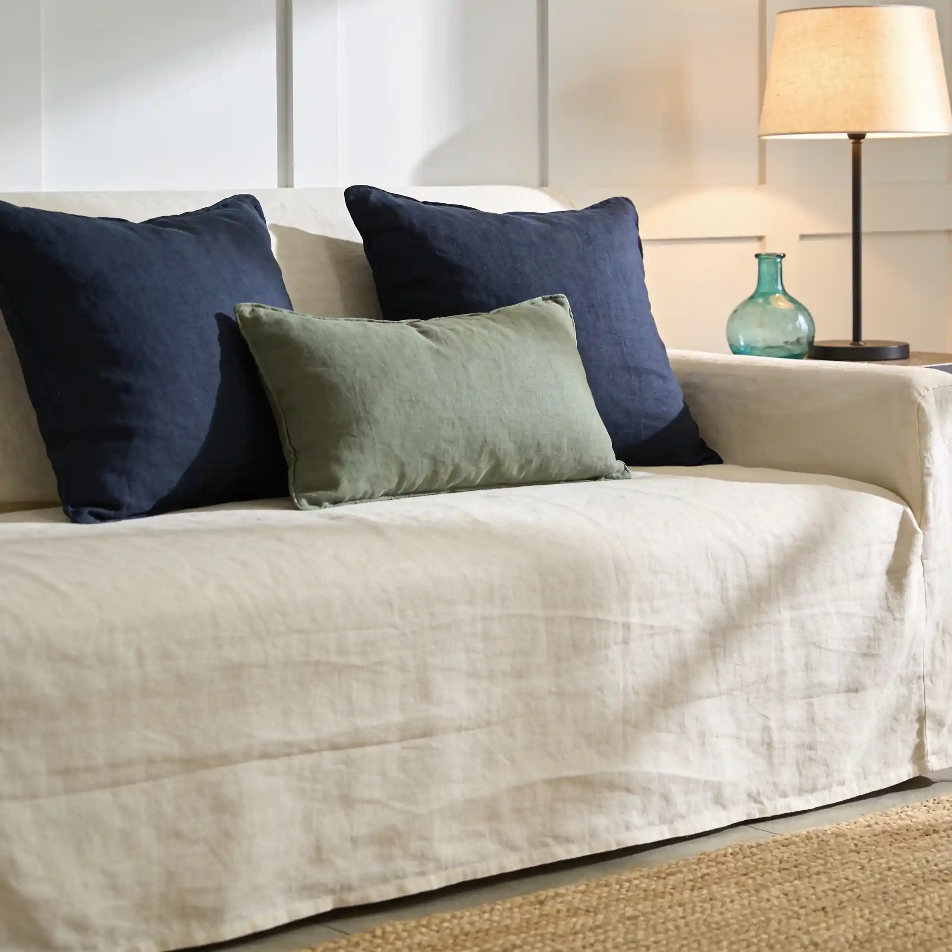 Coastal living room ideas: navy and sage pillows on cream linen sofa against soft white walls and natural jute rug