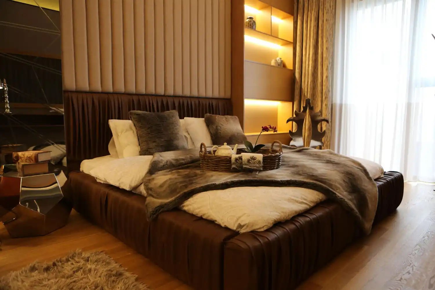 Warm luxurious bedroom with layered linen bedding, upholstered headboard, oak nightstand, and soft golden lamp light