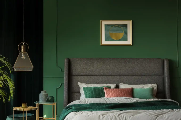 Moody dark academia bedroom with forest green walls, navy velvet headboard, antique brass sconces, and stacked books on the nightstand
