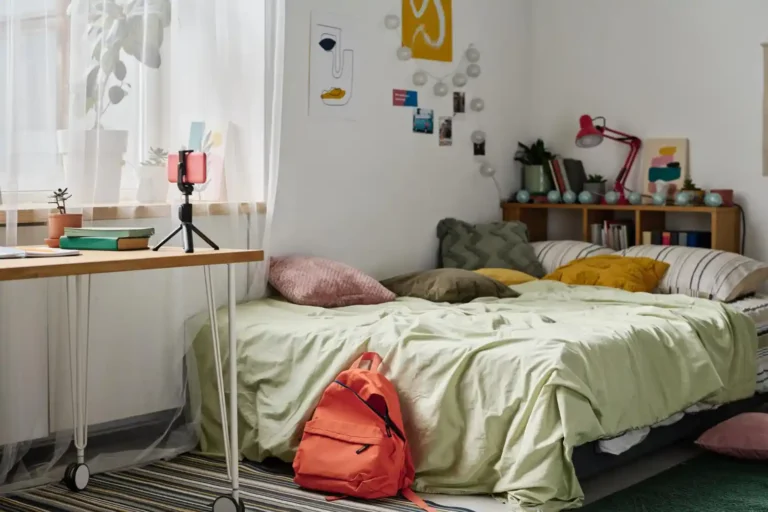 Cozy dorm room with a layered Twin XL bed in sage green and cream linen, decorative pillows, and a chunky knit throw