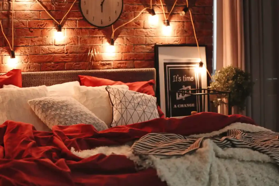 90s-inspired bedroom with a deep plum velvet headboard, burgundy plaid duvet, and warm string lights above a low platform bed