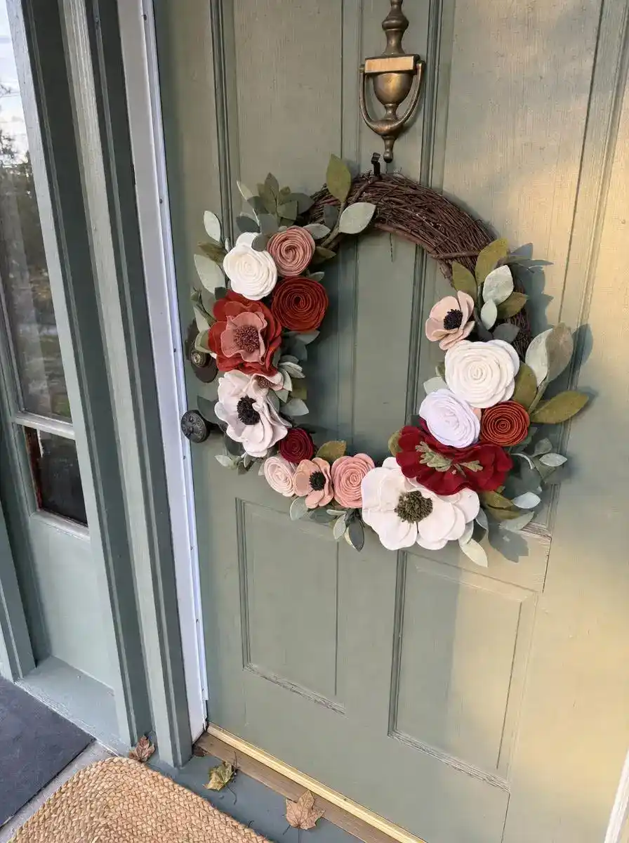 Felt flower wreath on a grapevine base hanging on a front door with greenery accents