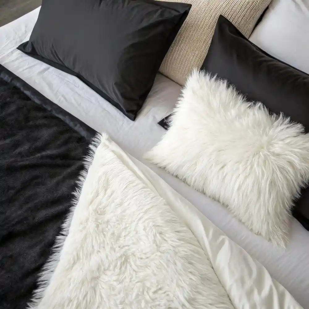 Layered bedding texture close-up mixing smooth sateen, washed linen, and a nubby boucle pillow in oat tones