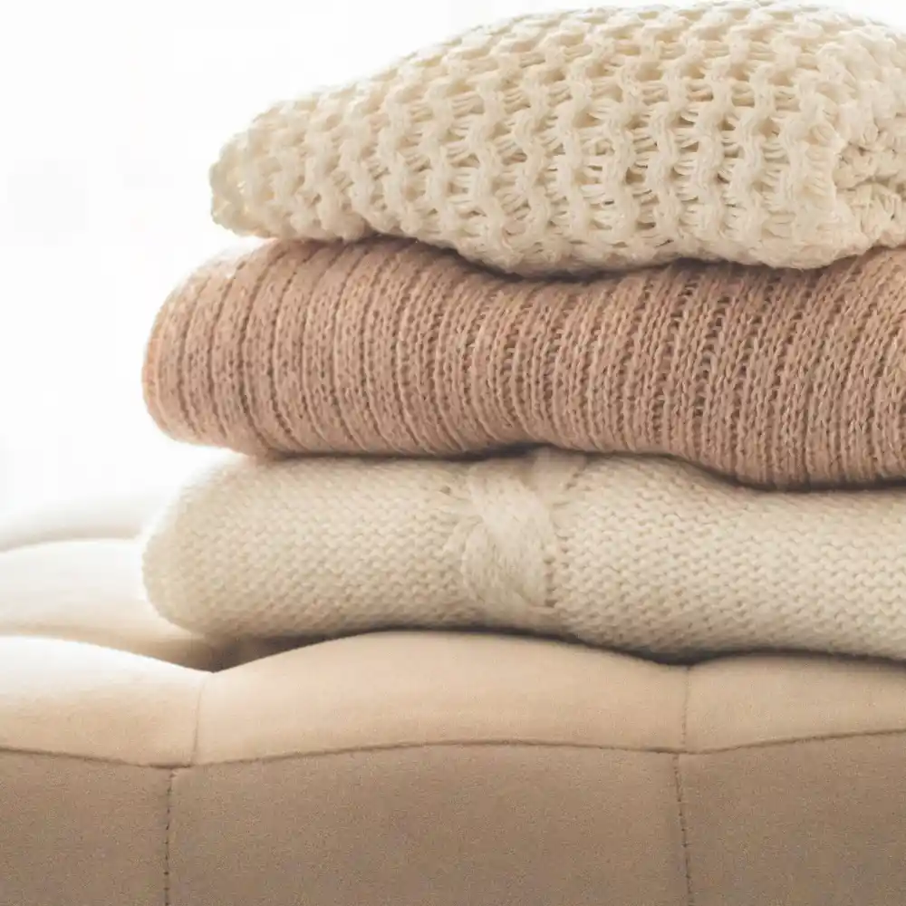 Close-up of deeply layered washed linen bedding in cream and oat with a folded knit blanket on a bed