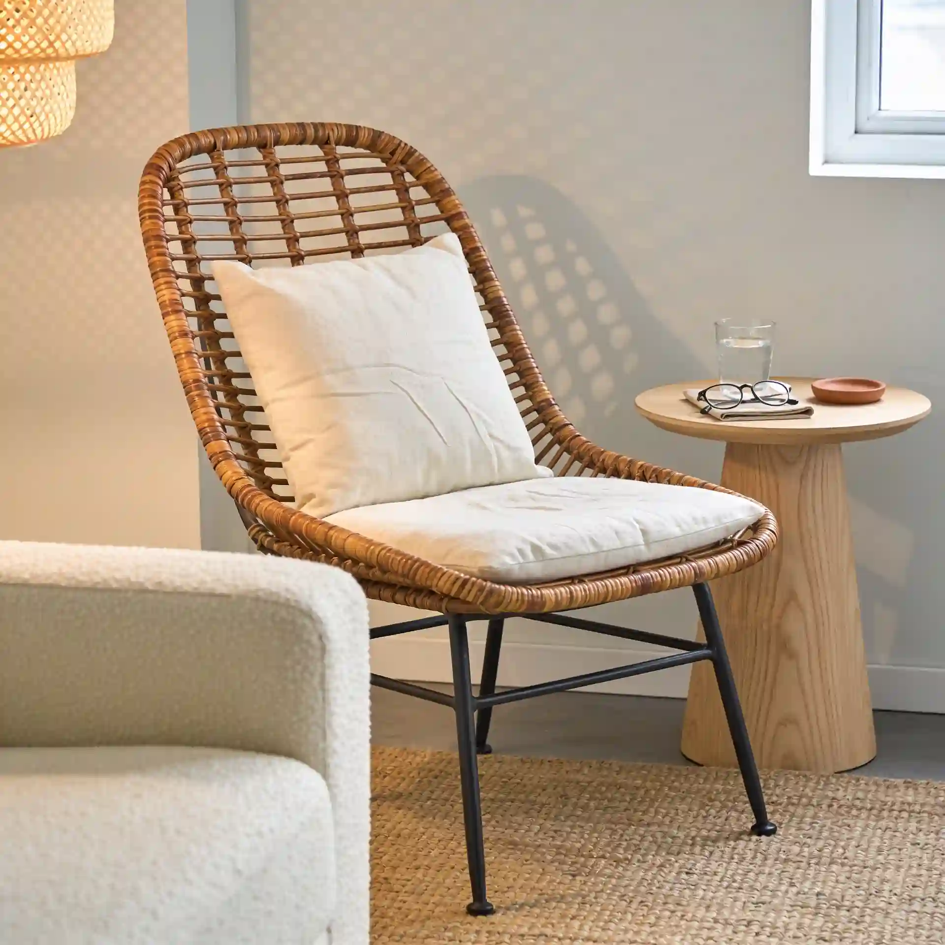 Rattan accent chair with cream linen cushion in a modern coastal living room beside a low-profile linen sofa on a honey jute rug
