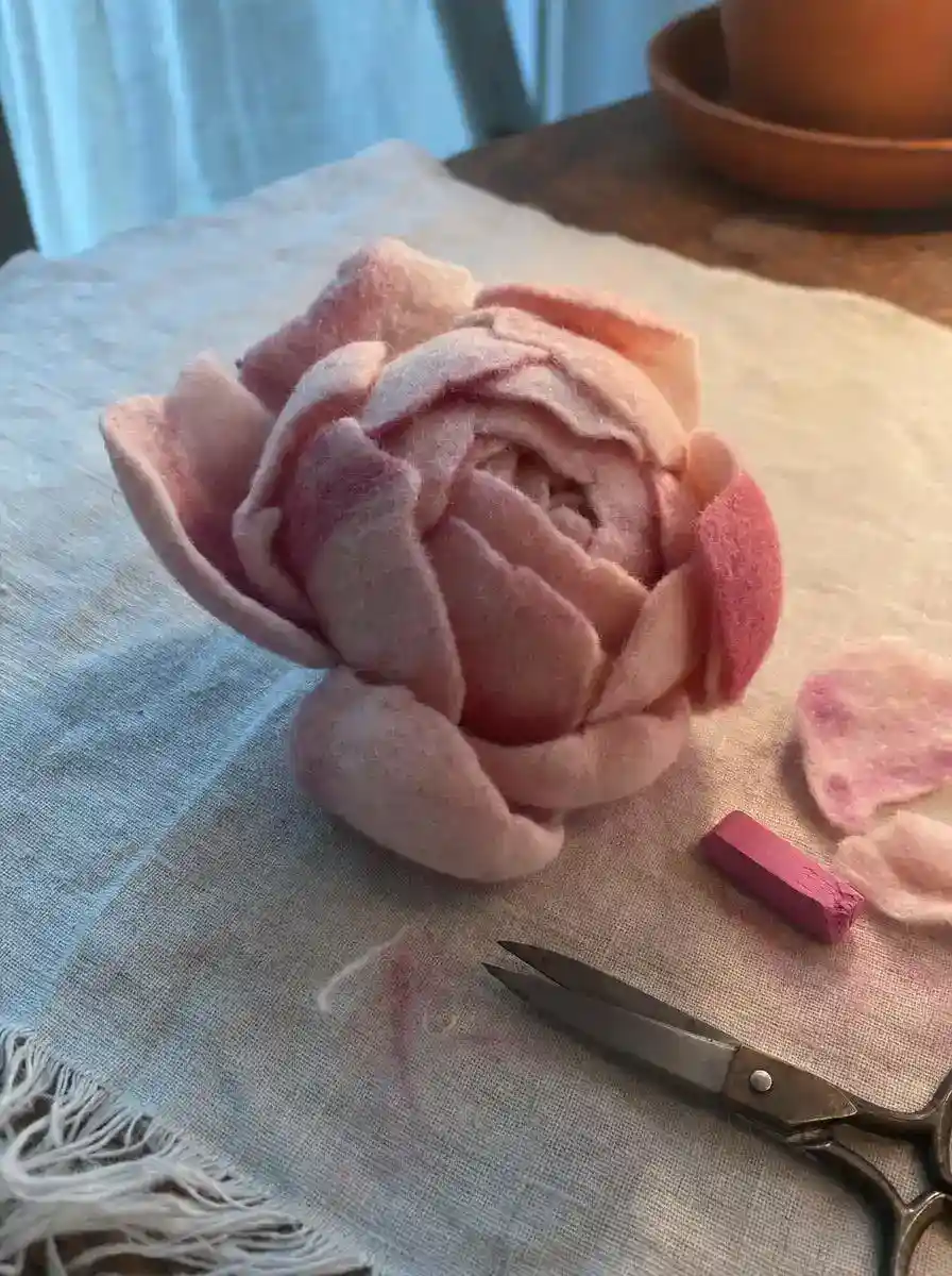 Close-up of a handmade felt peony showing cupped, layered petals with soft pink edge shading