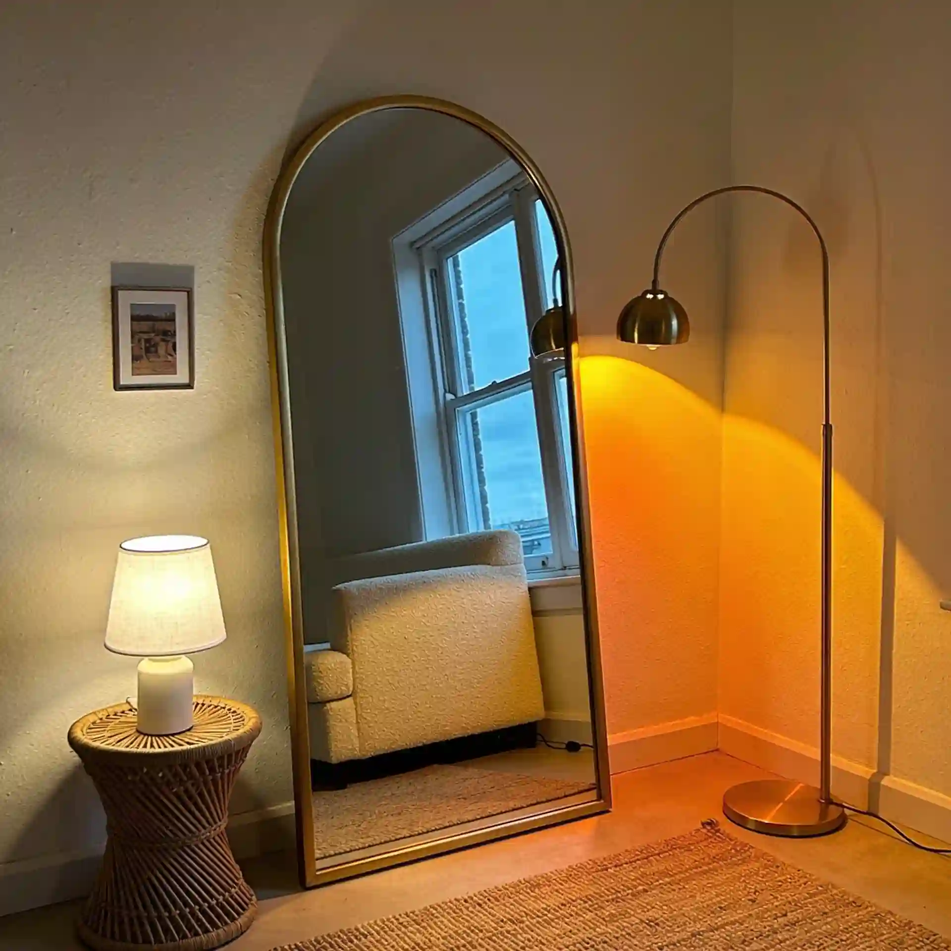 Small living room with three layered light sources — floor lamp, table lamp, and ceiling source — plus a large arched mirror reflecting window light