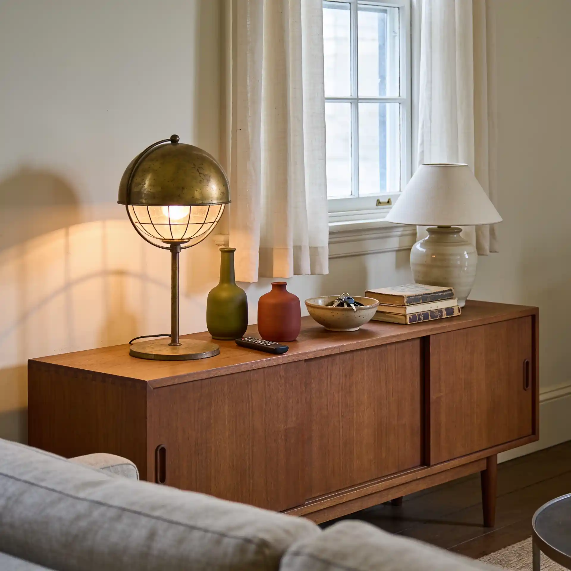 Mid century modern living room ideas shown with walnut console, cream sofa, and layered globe lighting
