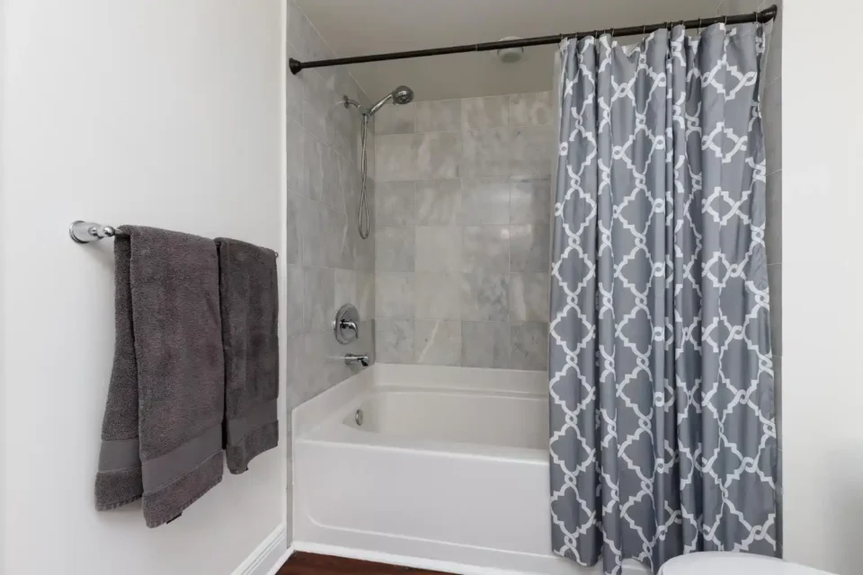 Bathroom with a long linen shower curtain hung near the ceiling over a white tub, brass rod and warm tile