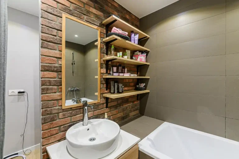 Modern bathroom with open floating oak shelves holding folded towels, jars, and a plant above the vanity
