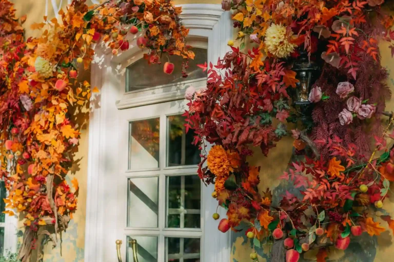 Front porch styled with a layered coir mat over a woven outdoor rug, dried wreath, white pumpkins, and warm lantern light