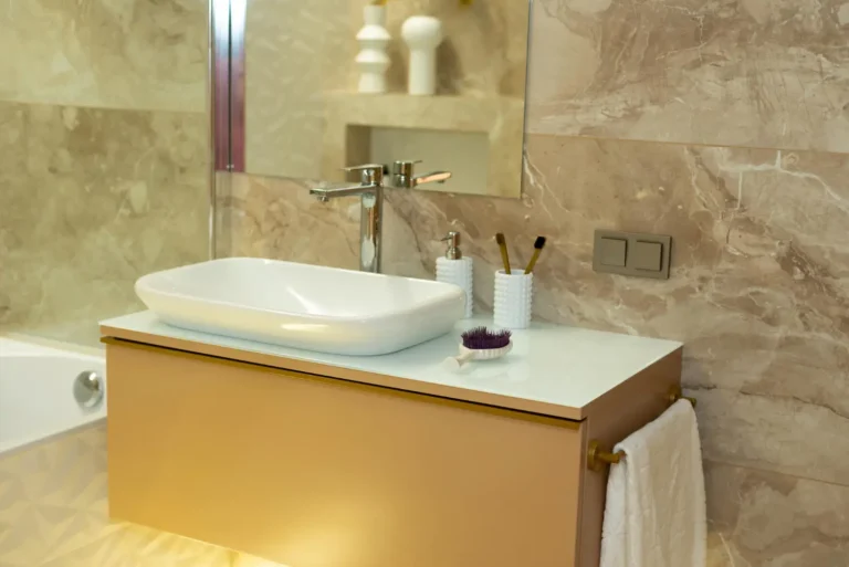 Warm neutral bathroom with beige marble walls, a tan floating vanity, a white vessel basin, and a brass towel bar