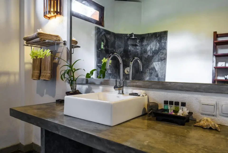 Industrial-style bathroom with a concrete vanity, matte black faucet, and warm walnut shelf against exposed brick